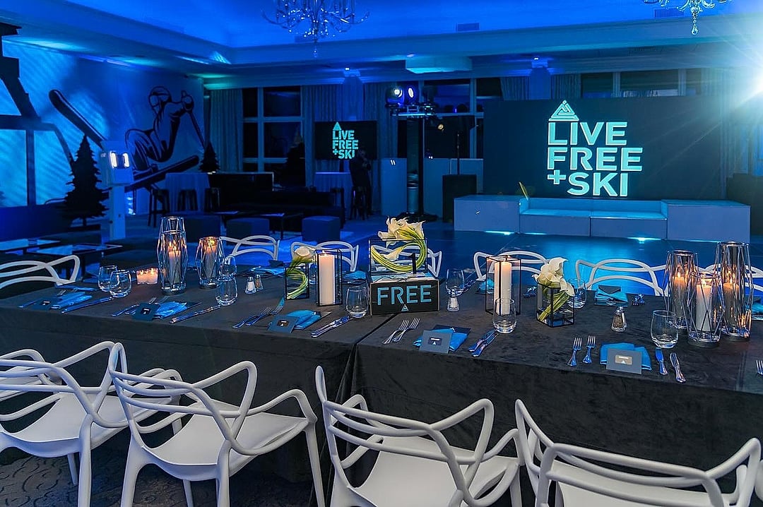 Long dining tables with white chairs beneath a ski-themed backdrop in blue light