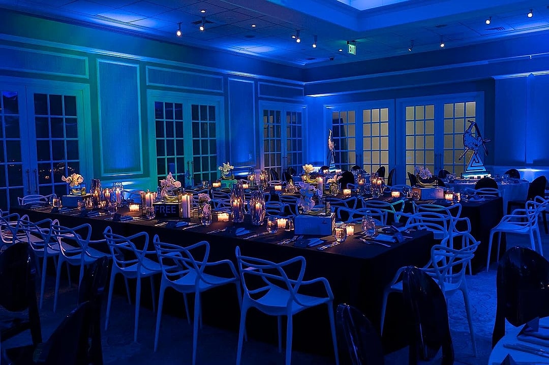 Ballroom of long dining tables glowing in deep blue uplighting
