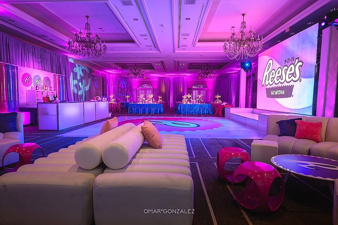 Ballroom in pink and purple light with white lounge seating and chandeliers