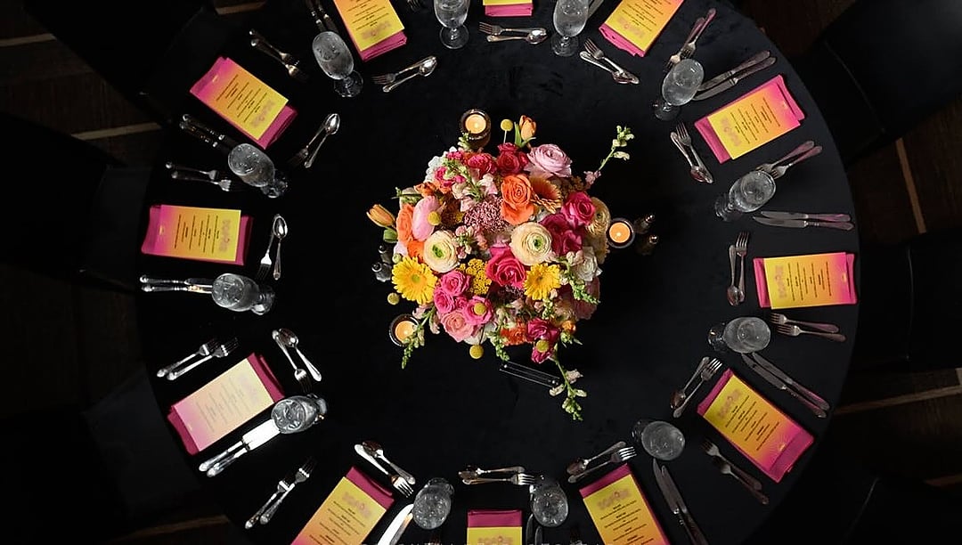 Overhead view of a black table set with a pink and orange floral centerpiece