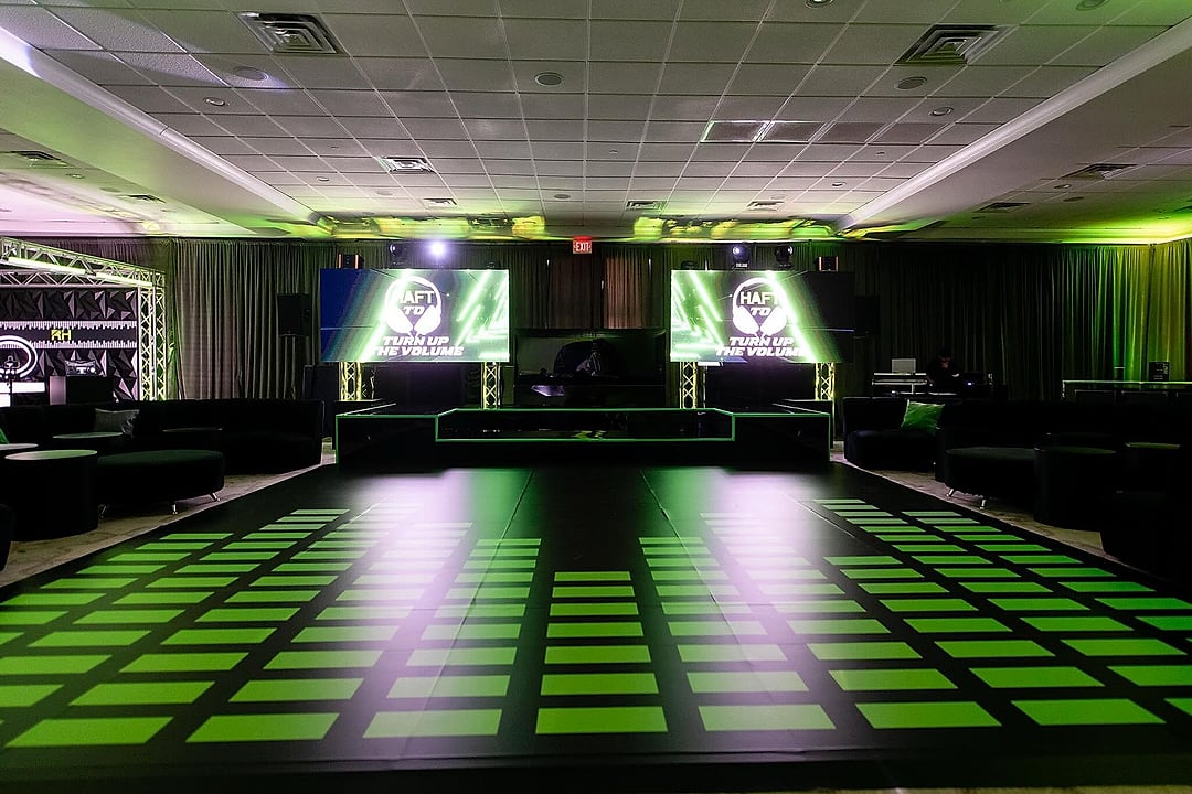 Dance floor of glowing green tiles beneath twin LED screens
